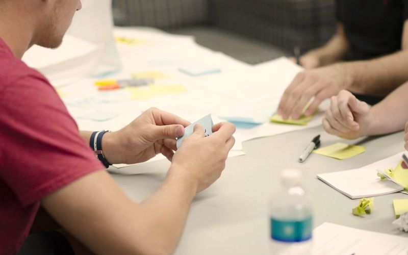 Mani che progettano insieme con fogli e post-it colorati su un tavolo