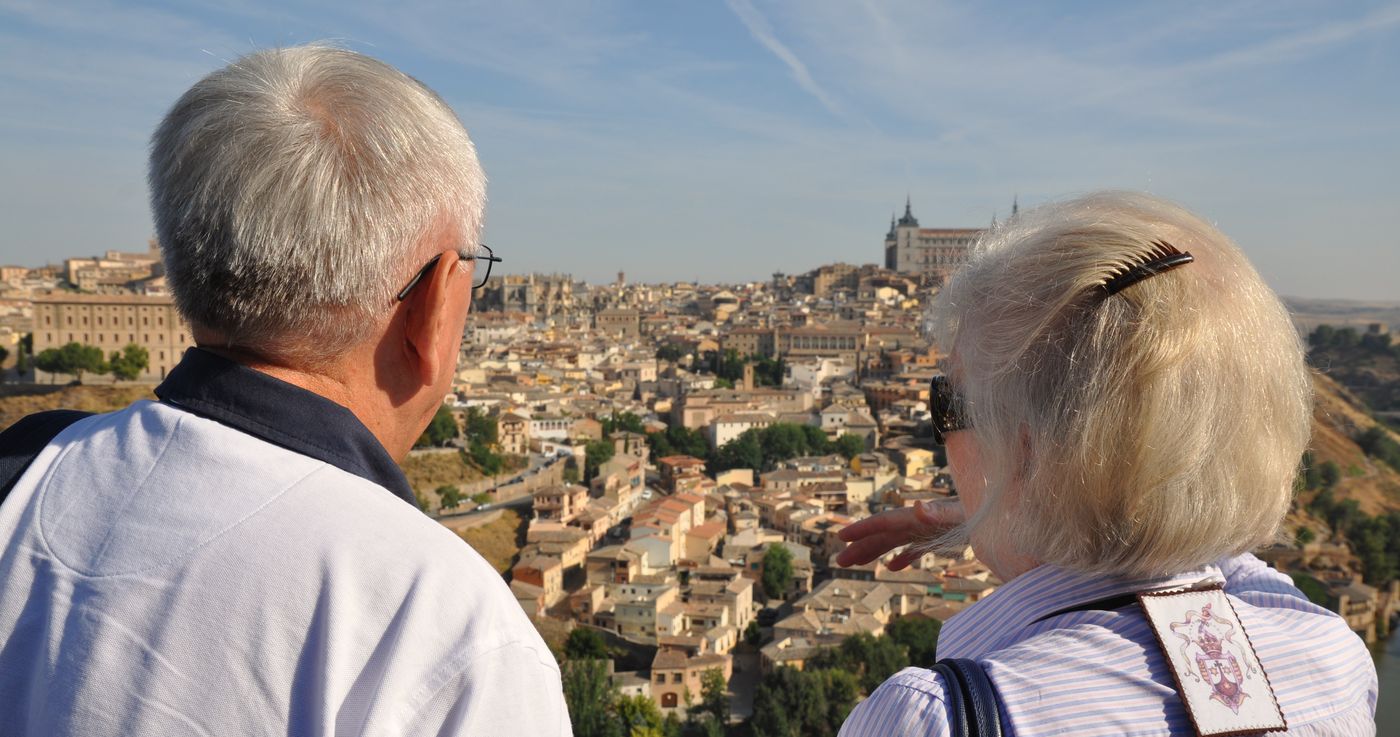 Una coppia di anziani, di spalle, guarda dall'alto i tetti di una città storica europea